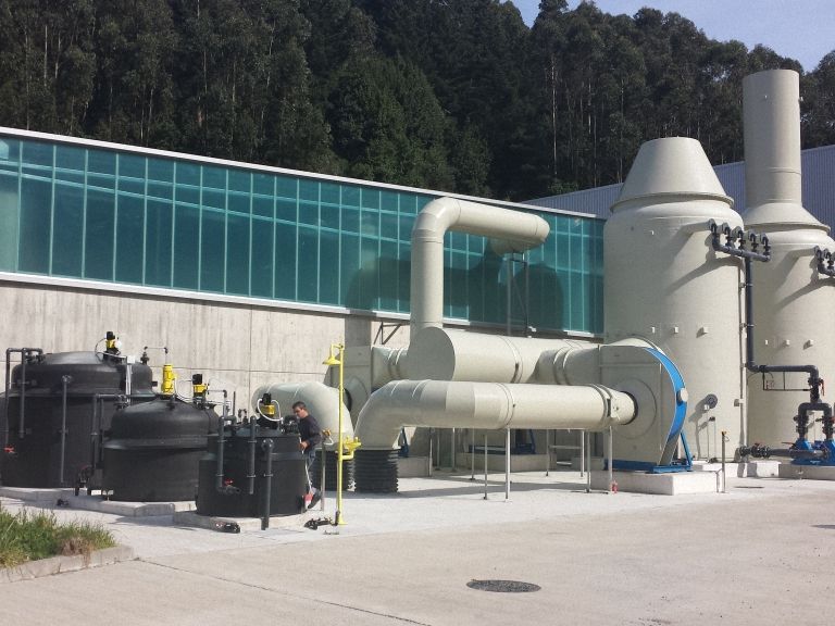 Instalación industrial con grandes tanques, tuberías y chimeneas con un fondo de árboles .