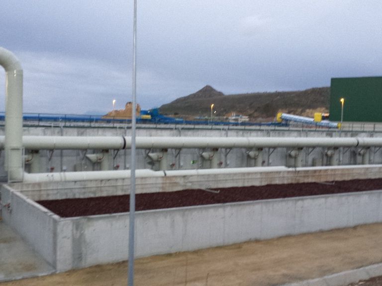 Una planta de tratamiento de agua con depósitos y tuberías de hormigón con una ladera de fondo bajo un cielo nublado.