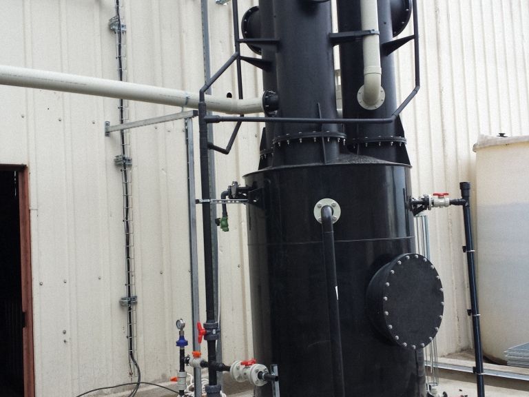 Torre de tratamiento de agua industrial negra con tuberías y válvulas fuera de un edificio.