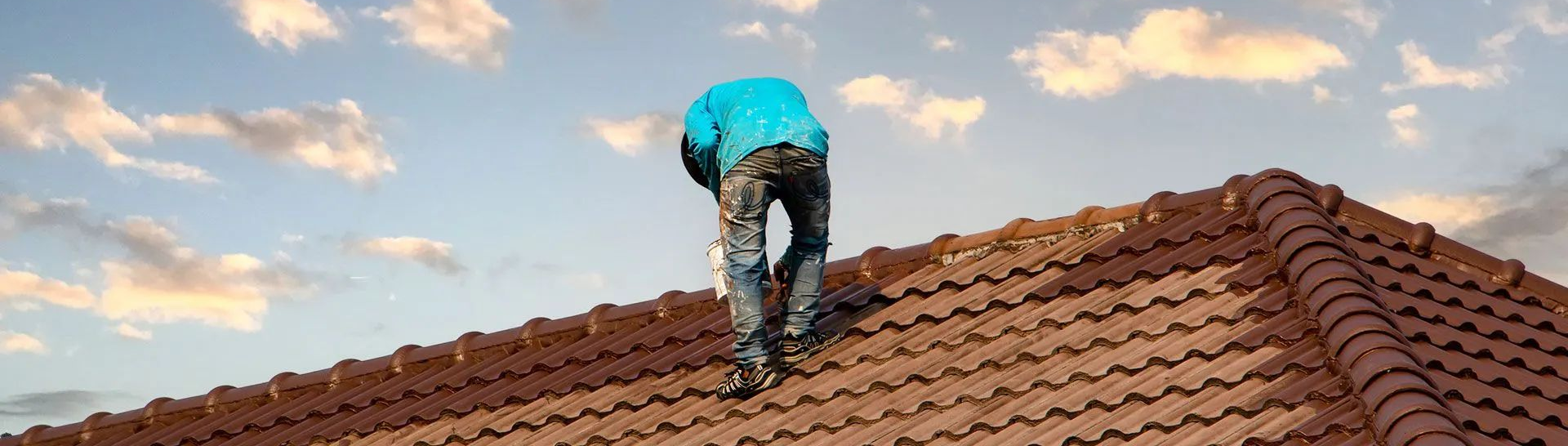 Une personne vêtue d'une veste bleu vif travaille sur un toit de tuiles