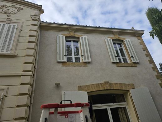 Vue en contre-plongée de l'extérieur d'un bâtiment beige avec deux fenêtres à volets blancs et une échelle au premier plan.