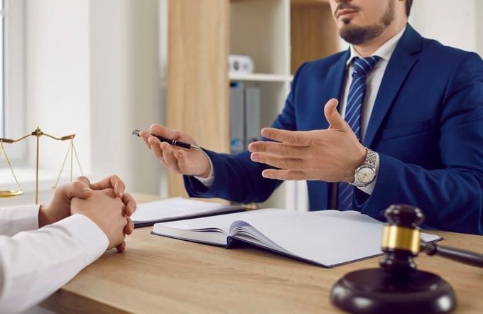Un hombre con traje y corbata está sentado en un escritorio hablando con otro hombre.