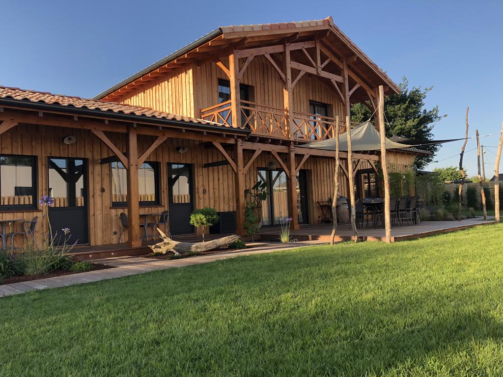 Maison en bois à deux étages avec porche et balcon, située sur une pelouse herbeuse sous un ciel bleu.