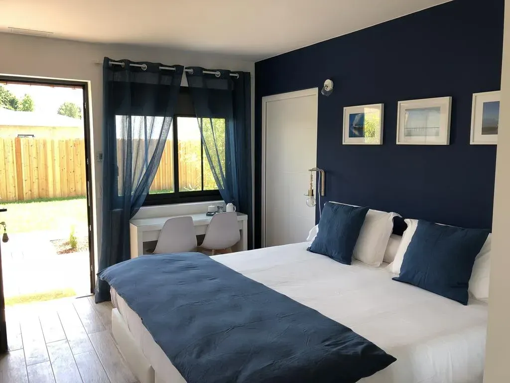 Chambre avec un mur d'accent bleu, un lit avec des touches de bleu, une fenêtre avec des rideaux transparents et un bureau.