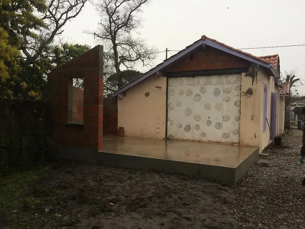 Un bâtiment en construction, aux murs de briques et de stuc apparents, sous un ciel couvert.