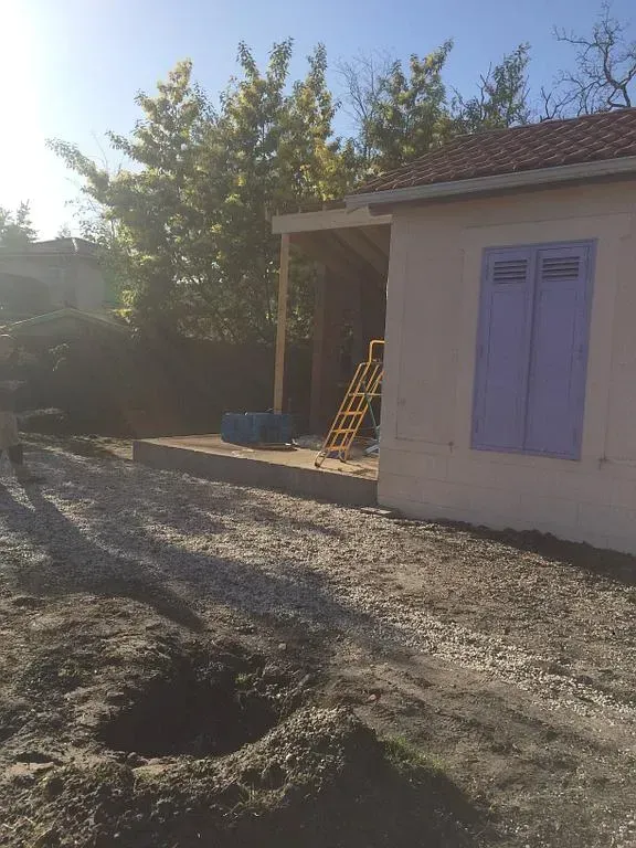 Maison en construction avec volets violets, cour en gravier et porche.