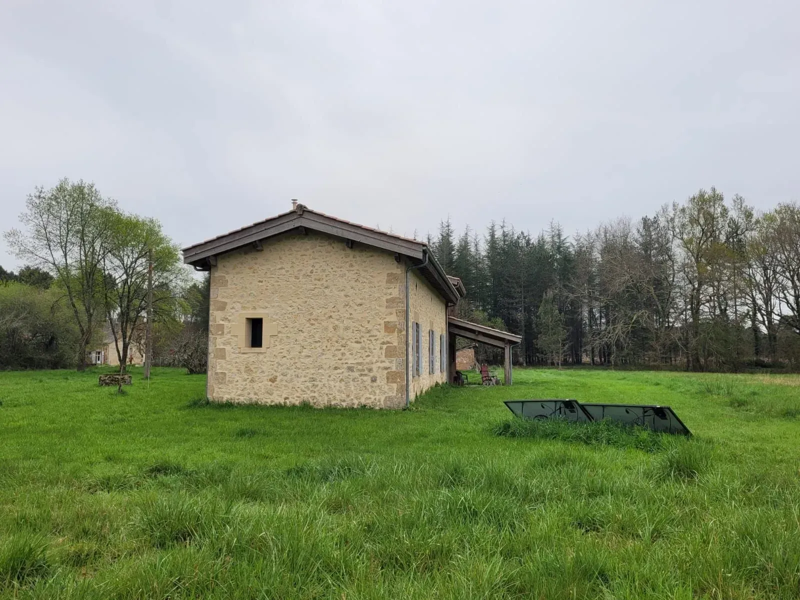 Un bâtiment en pierre au toit en pente se dresse au milieu d'un champ herbeux sous un ciel nuageux.