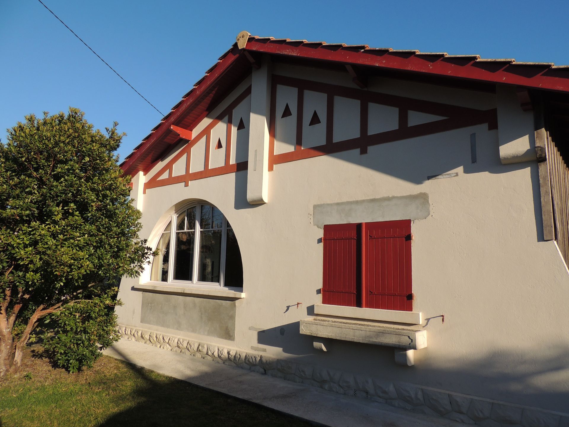 Une maison au toit rouge, aux volets et aux poutres décoratives en bois, sous un ciel bleu.