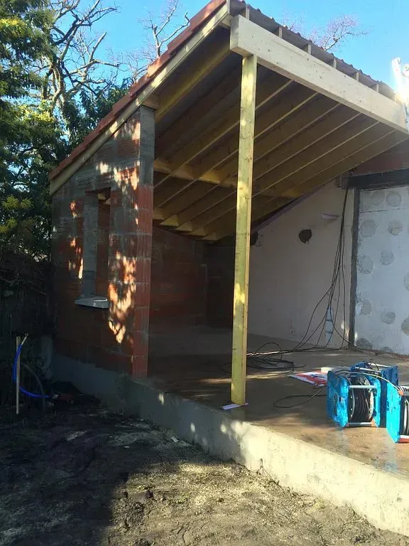 Construction d'une structure en briques rouges et en bois avec une base en béton ; toiture partiellement achevée ; cadre extérieur ensoleillé.