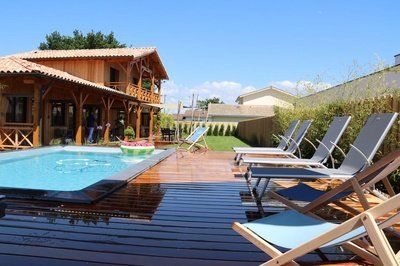 Maison en bois avec piscine et terrasse, chaises longues installées, ciel bleu.