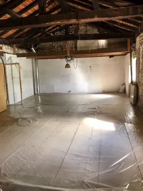 Pièce intérieure avec plafond à poutres apparentes, revêtement de sol en plastique et murs blancs.