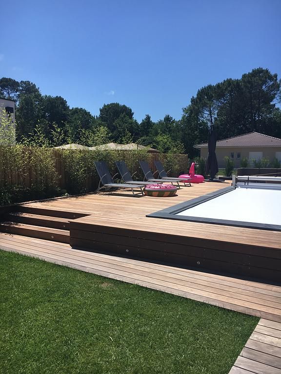 Terrasse en bois avec piscine, chaises longues et flamant rose gonflable ; pelouse et arbres en arrière-plan.