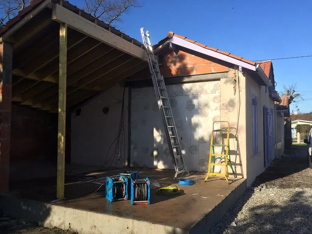 Chantier de construction avec extension de porche à ossature bois sur fondation en béton, échelle et équipement.