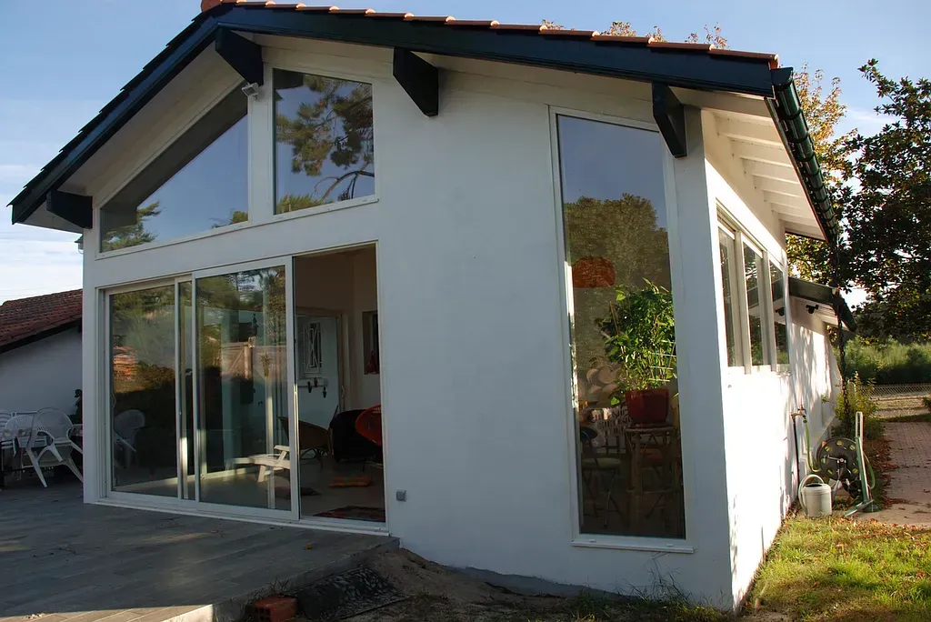 Maison blanche avec de grandes baies vitrées et des portes coulissantes, patio et ciel bleu.