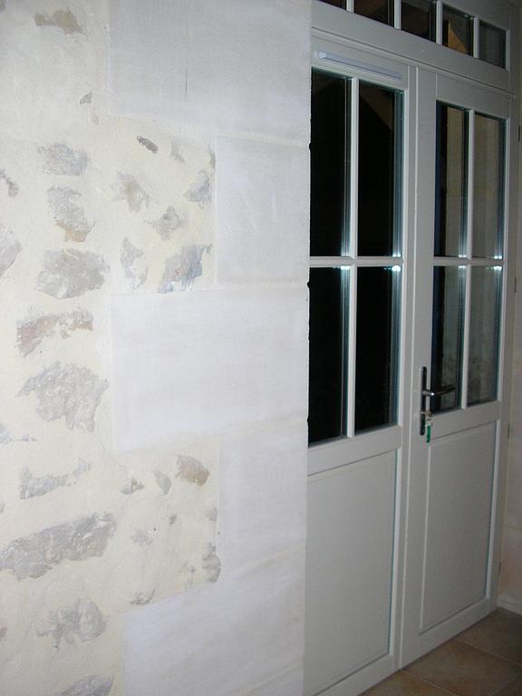 Un mur en pierre jouxte une double porte vitrée, le tout peint en blanc.