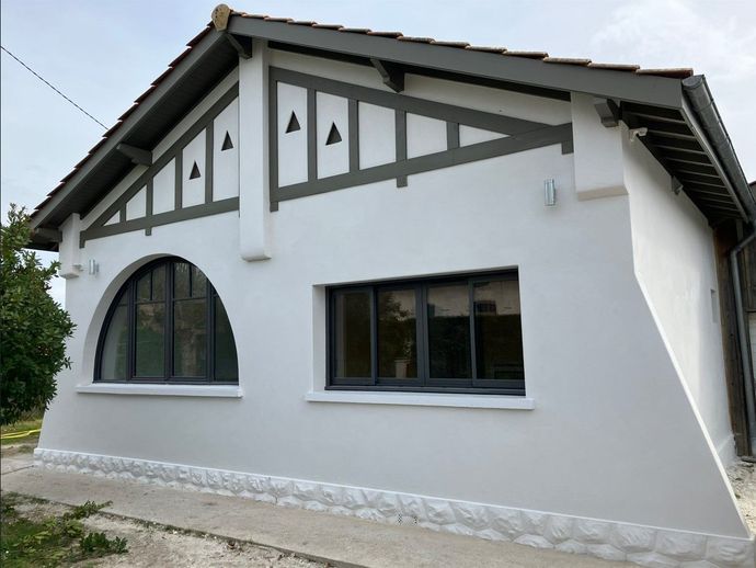 Maison blanche avec des garnitures grises, dotée d'une fenêtre cintrée et d'un toit à pignon.