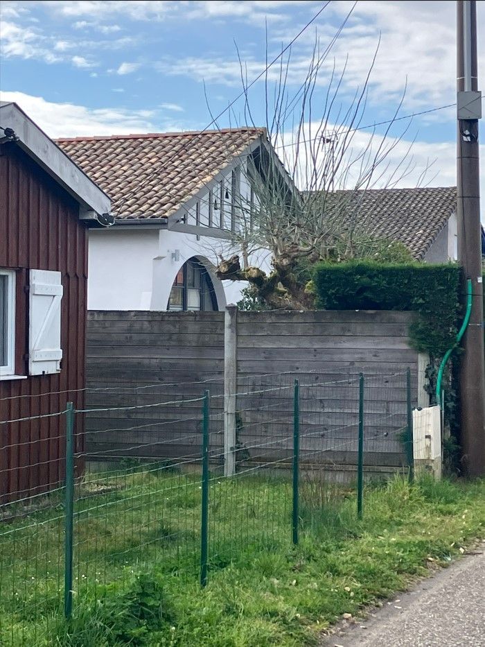 Des maisons derrière une clôture en bois et une clôture en fil de fer vert, sous un ciel nuageux.