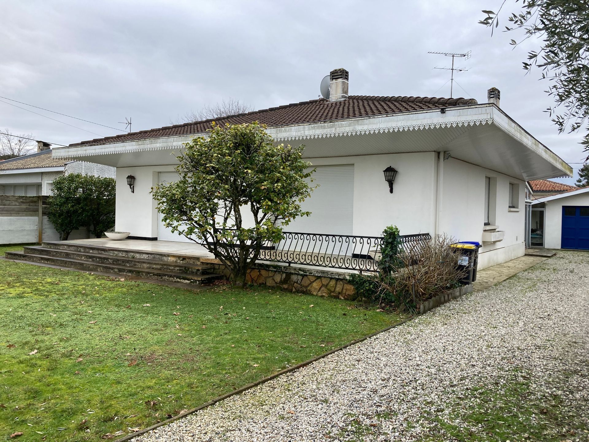 Maison blanche au toit brun et à la pelouse verte par temps nuageux. Allée de gravier.
