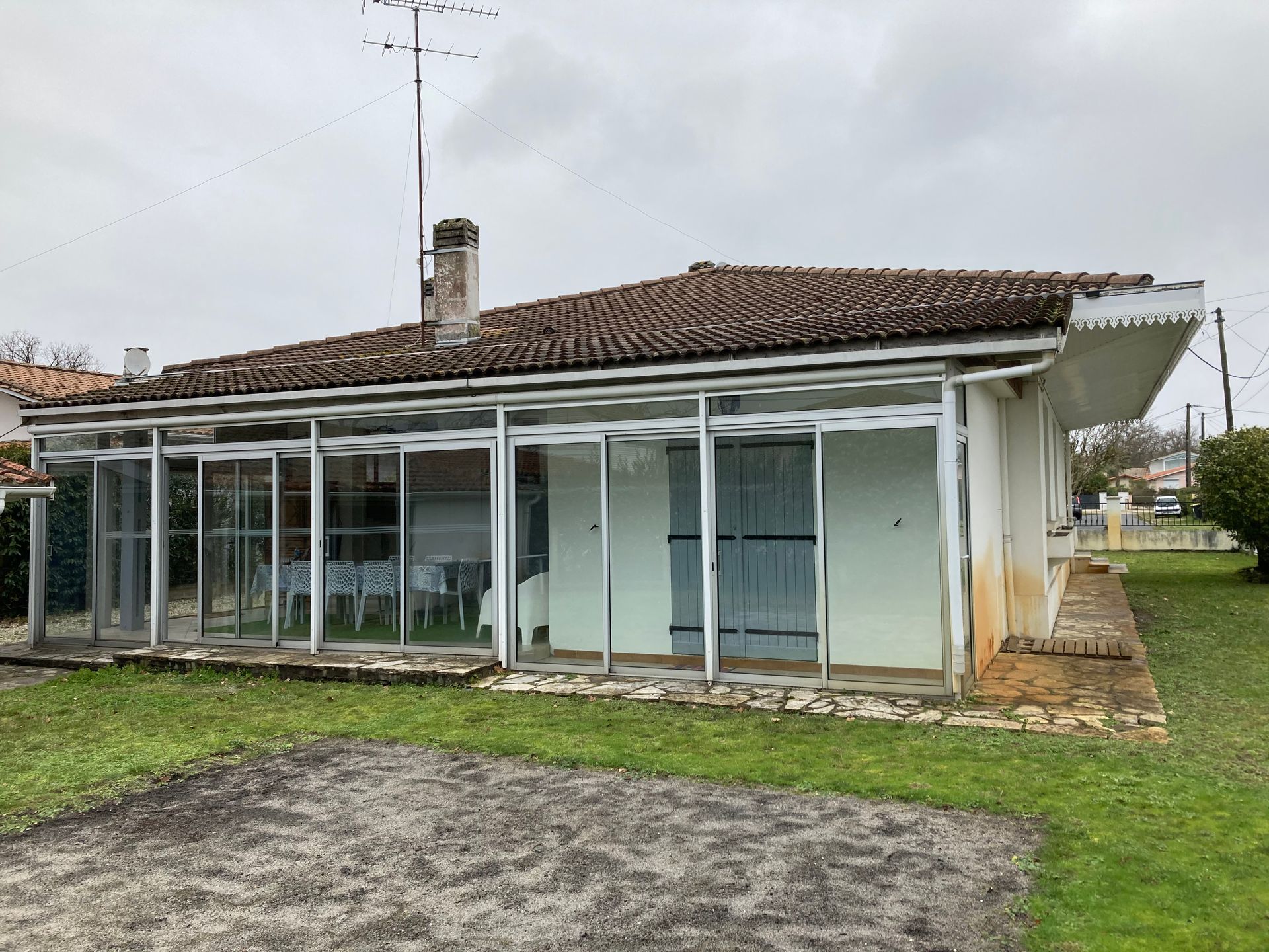 Maison de plain-pied avec une véranda vitrée sous un toit de tuiles, située sur une pelouse sous un ciel couvert.