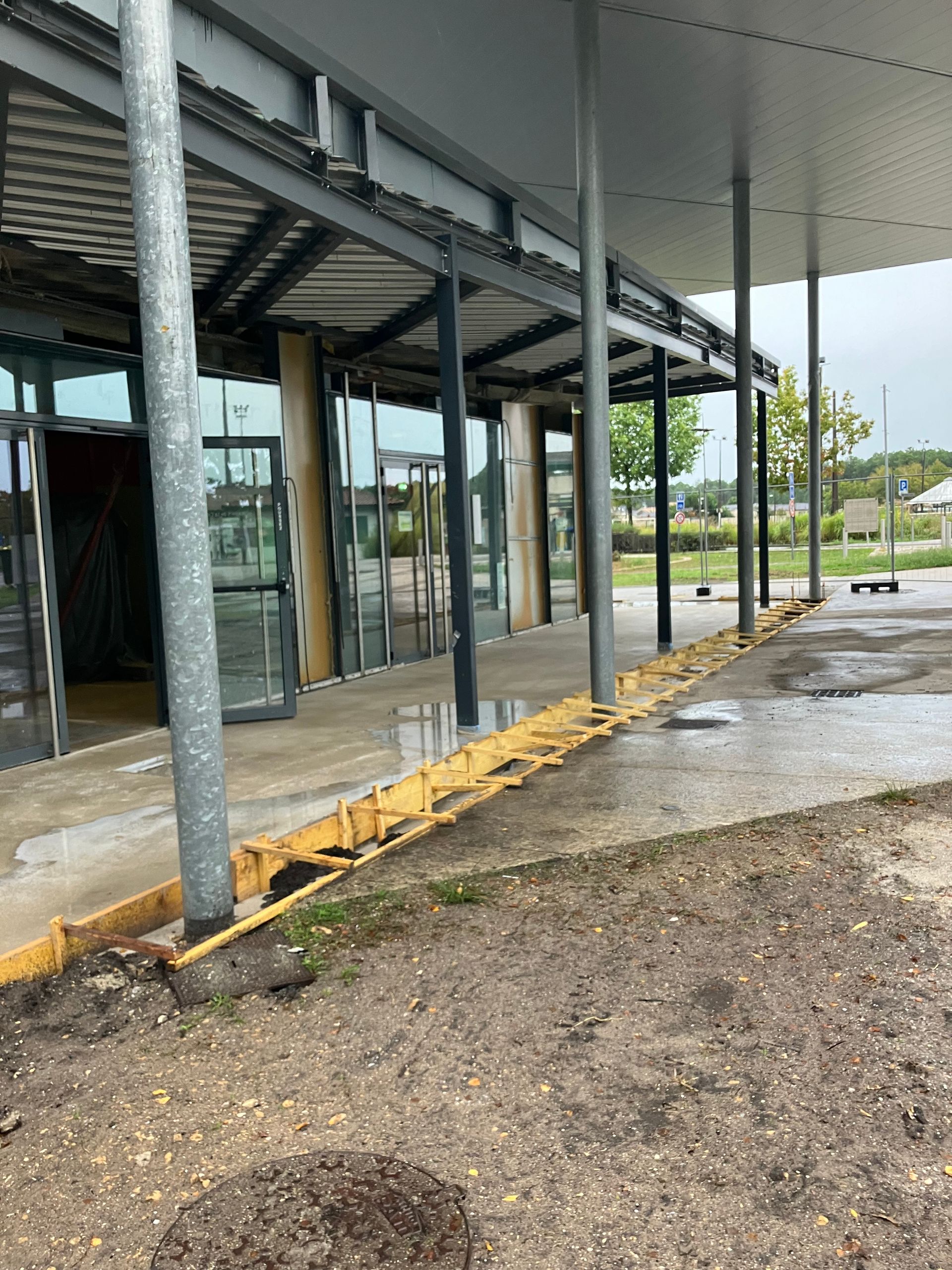 Extérieur d'un bâtiment en construction, doté d'un auvent soutenu par des poteaux métalliques.