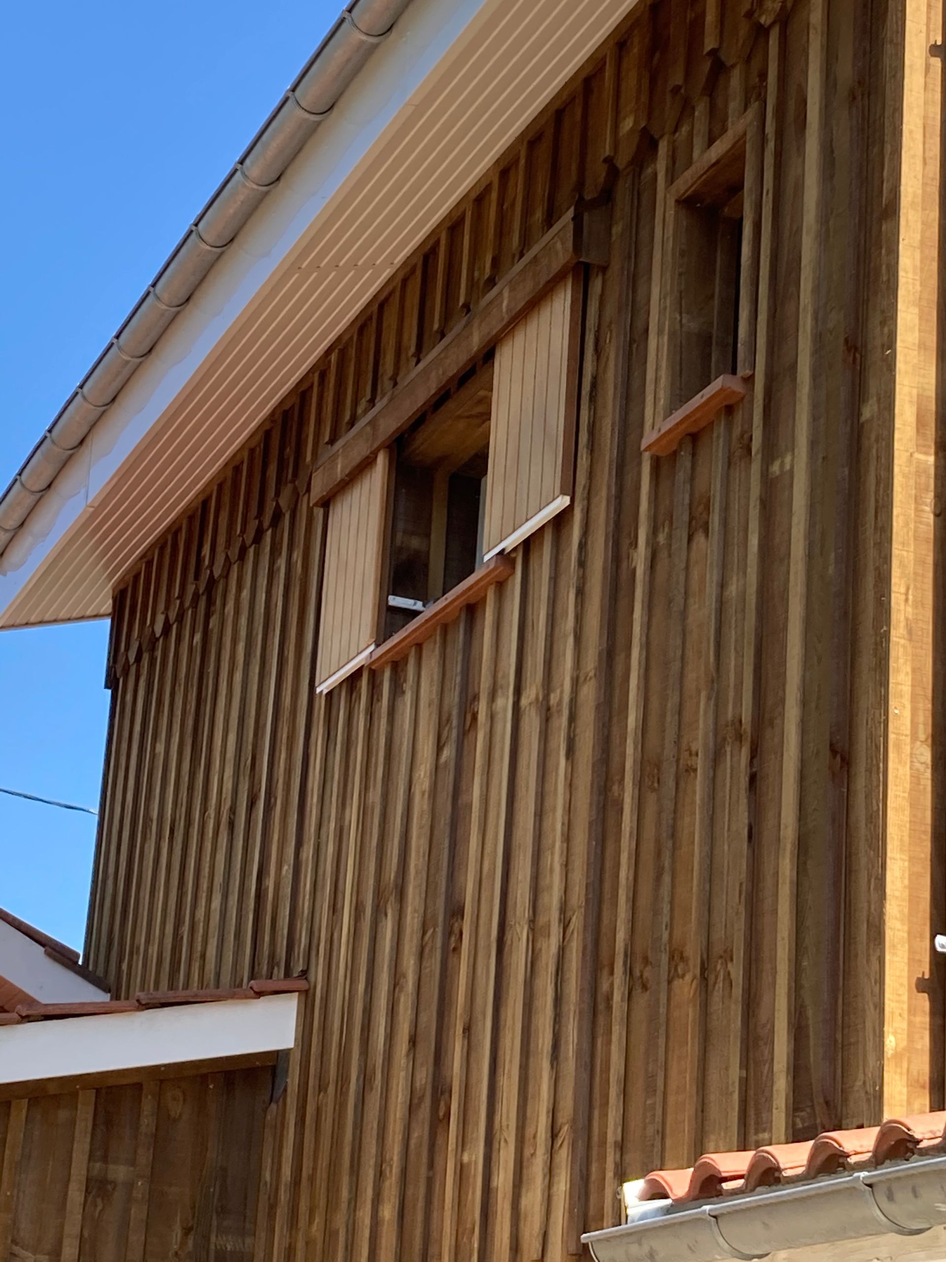 Bâtiment en bois avec deux fenêtres sous un avant-toit blanc, se détachant sur un ciel bleu.