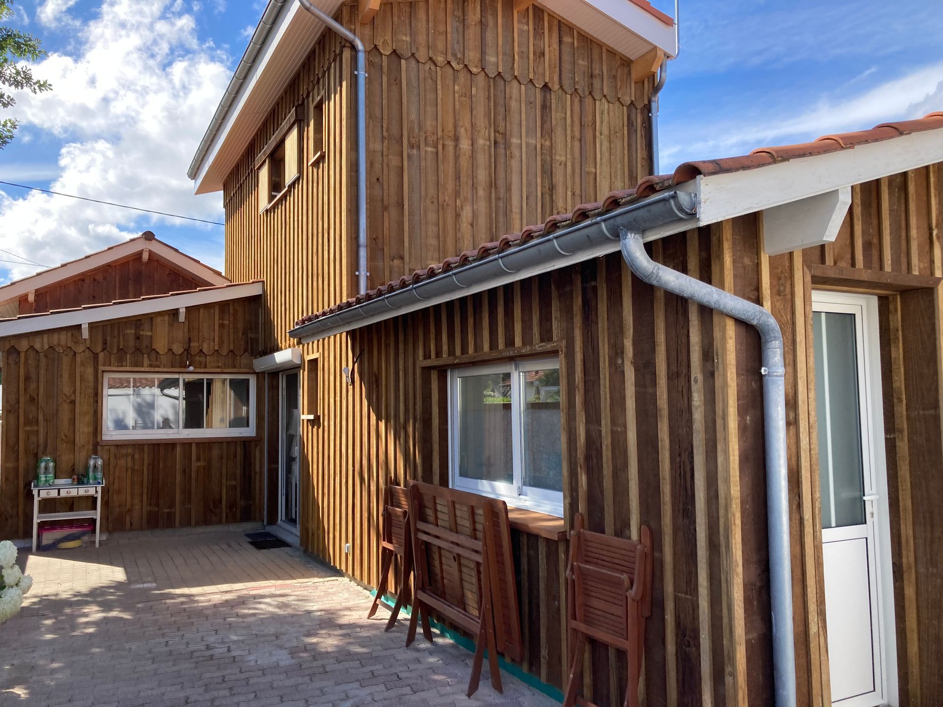 Extérieur de cabane en bois avec des garnitures blanches, des gouttières grises et un toit de tuiles rouges.