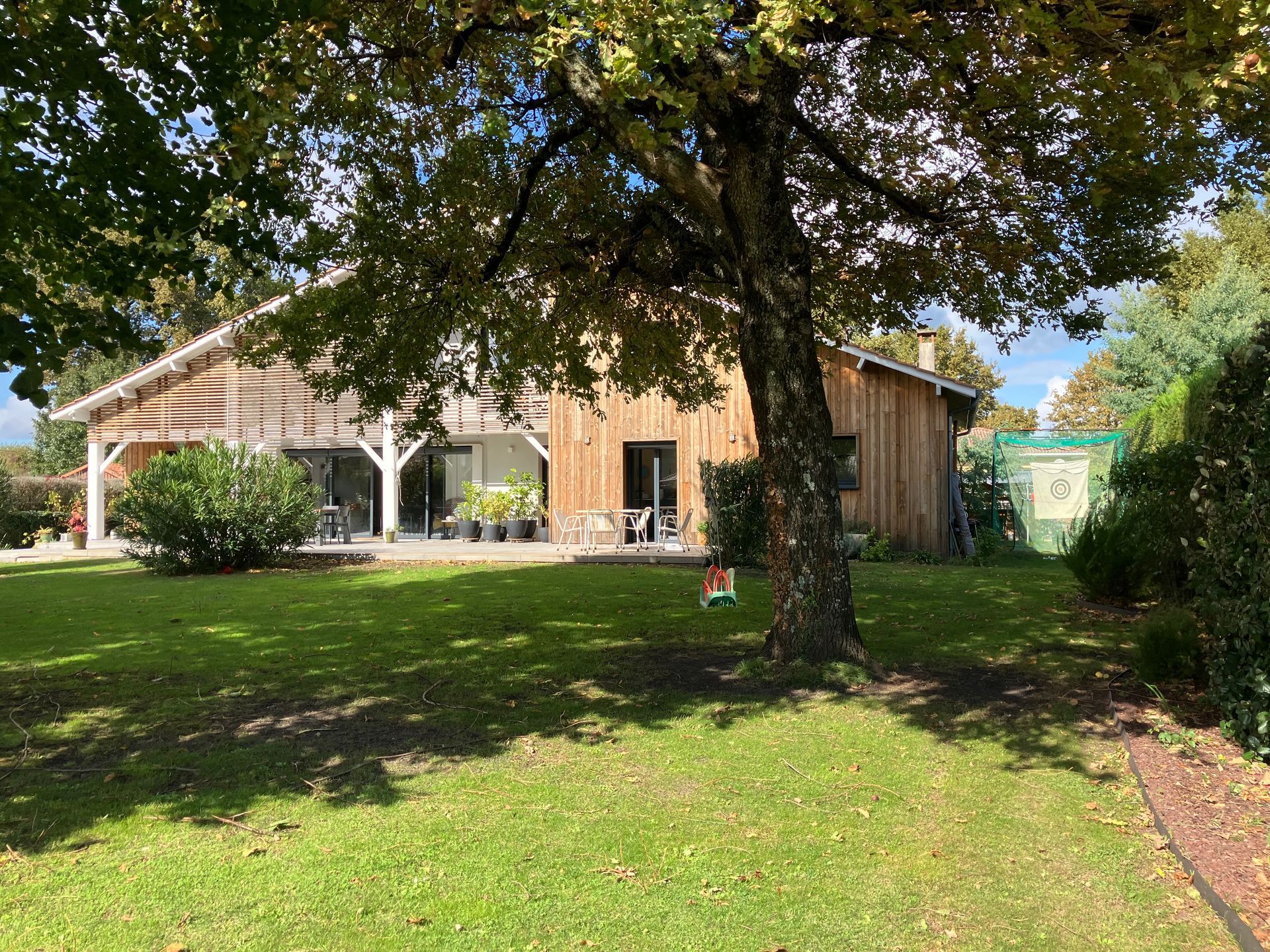 Maison en bois avec une pelouse et un arbre au premier plan.