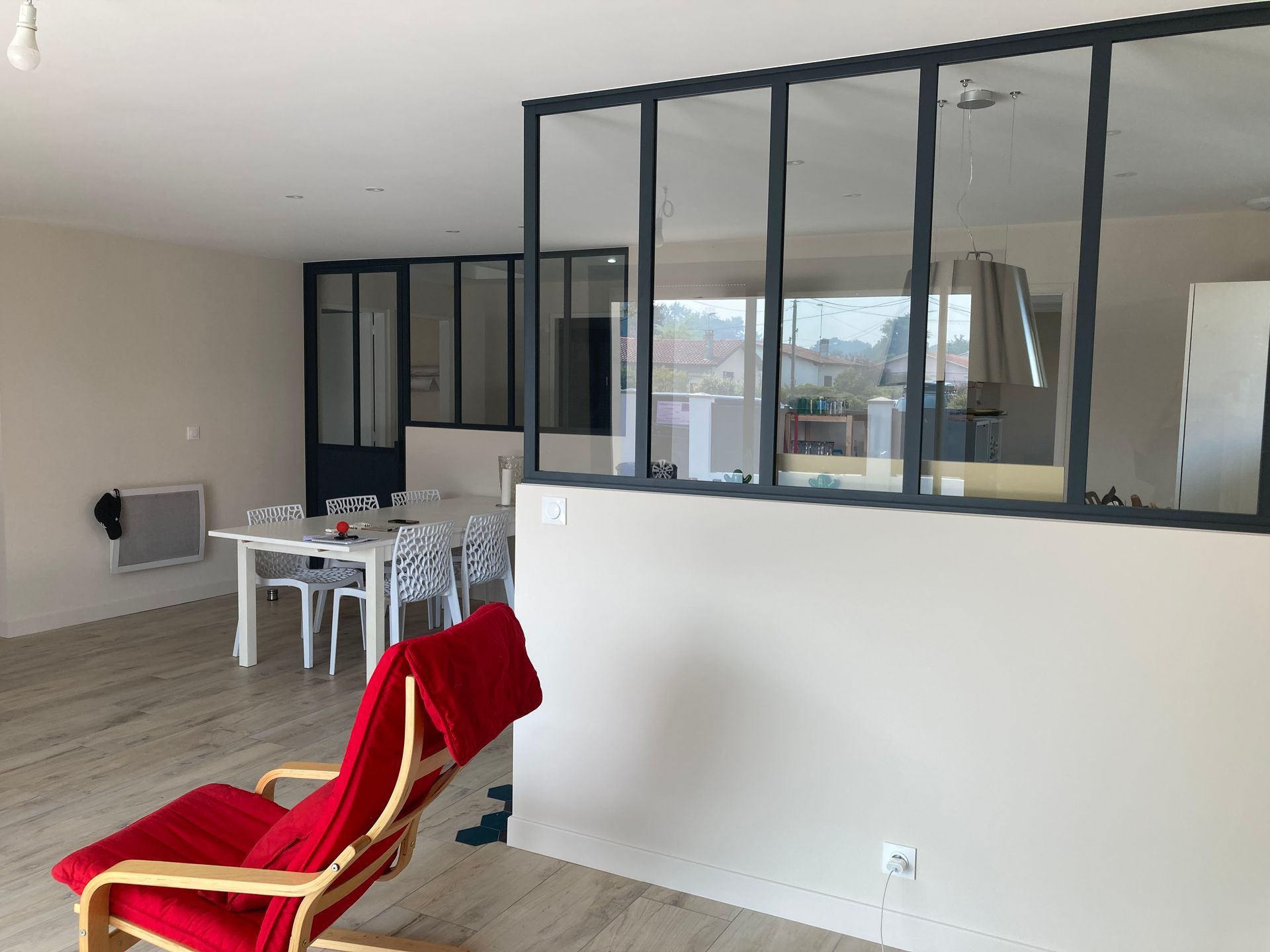 Chaise rouge dans une pièce baignée de lumière, avec une cloison vitrée séparant la salle à manger du salon.