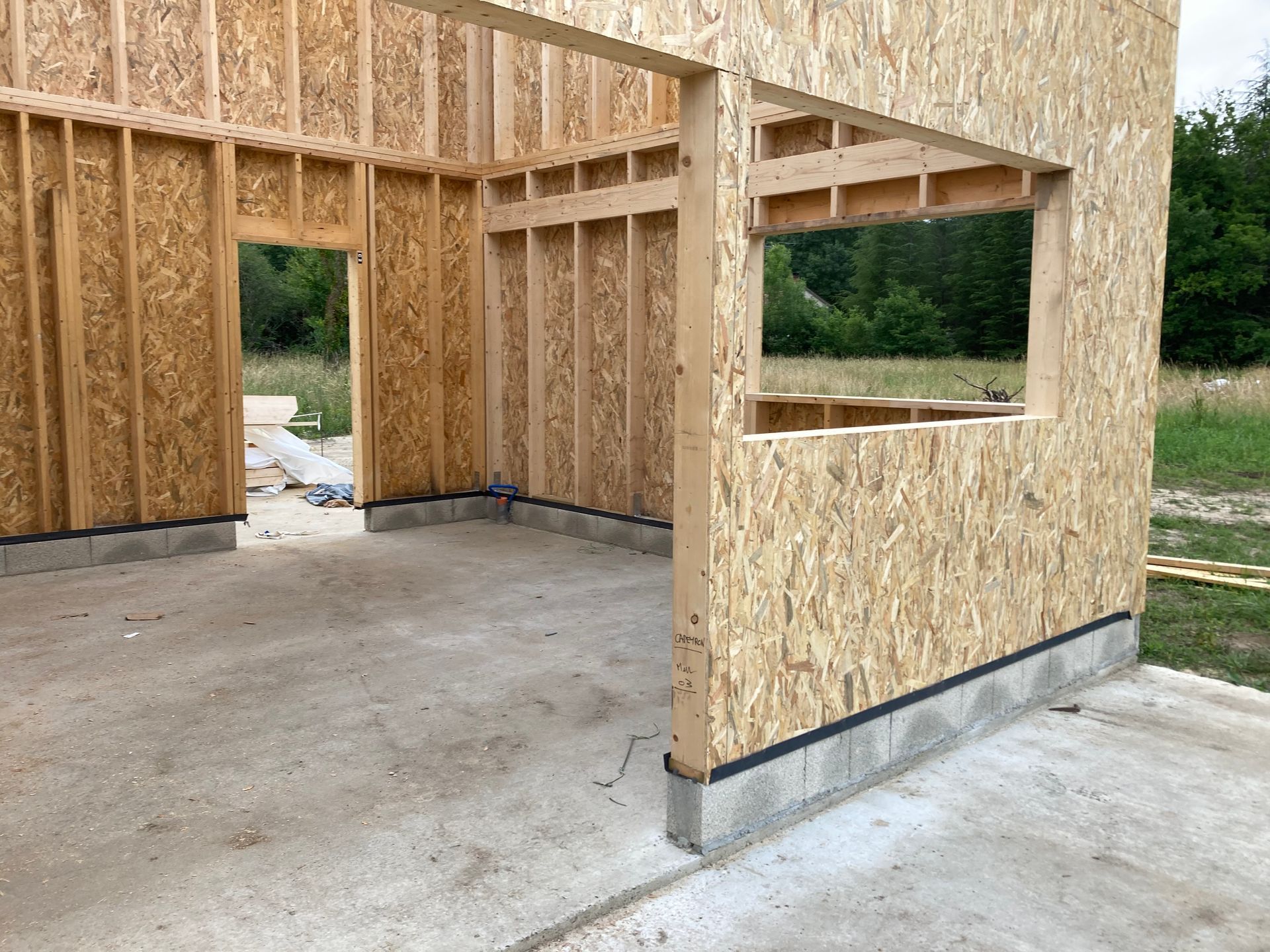 Ossature d'un nouveau bâtiment en construction, montrant le revêtement en panneaux OSB sur une fondation en béton.