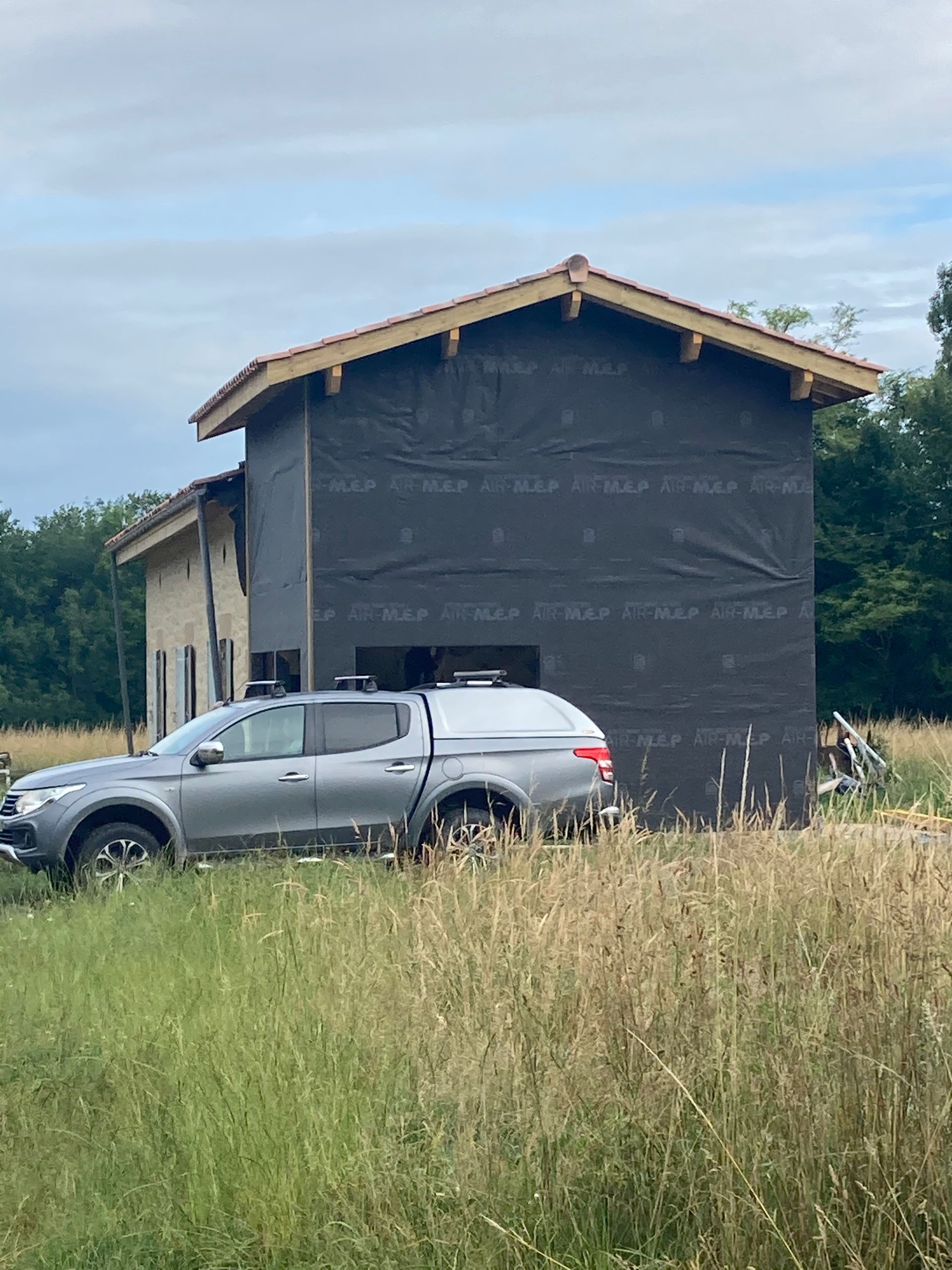 Une camionnette grise garée devant un bâtiment en construction, recouvert d'un matériau noir.
