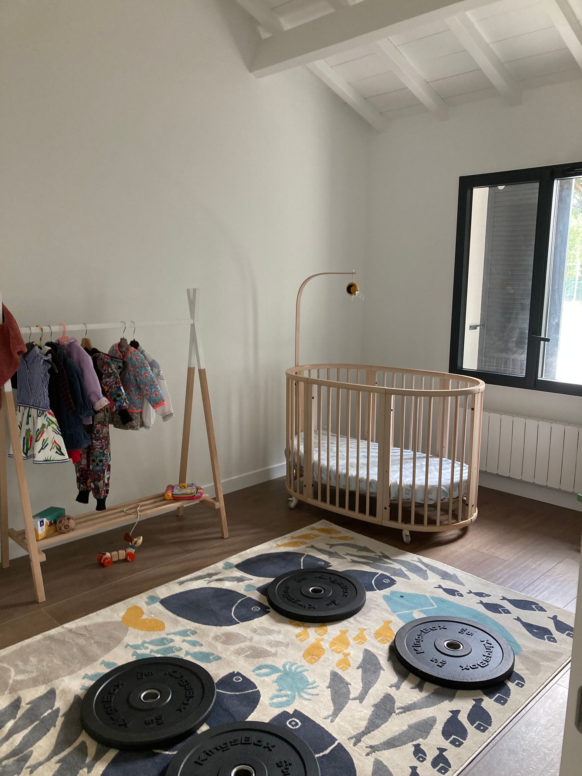 Chambre de bébé avec berceau, portant à vêtements et haltères au sol.
