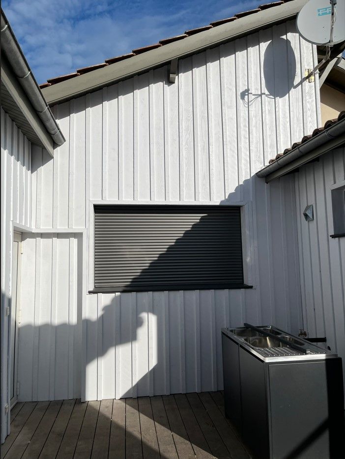 Bâtiment en bois blanc avec un volet noir fermé et une antenne parabolique.