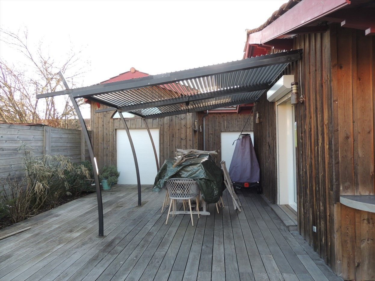 Pergola sur terrasse en bois attenante à un bâtiment en bois ; aménagement extérieur.
