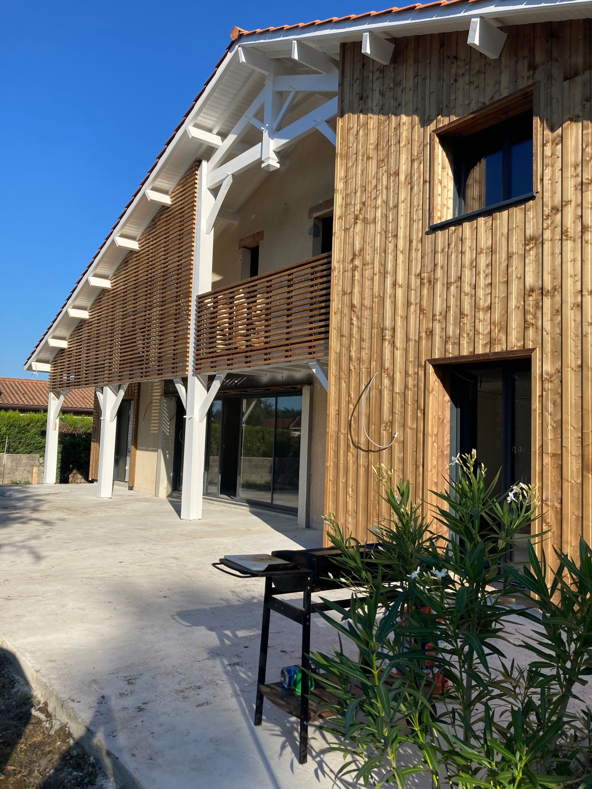 Maison en bois à deux étages avec véranda ouverte, balcon et ciel bleu dégagé.