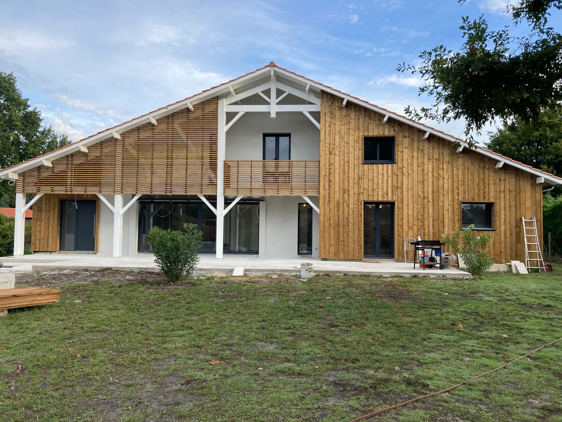 Maison en construction, façade blanche et bardage en bois naturel.