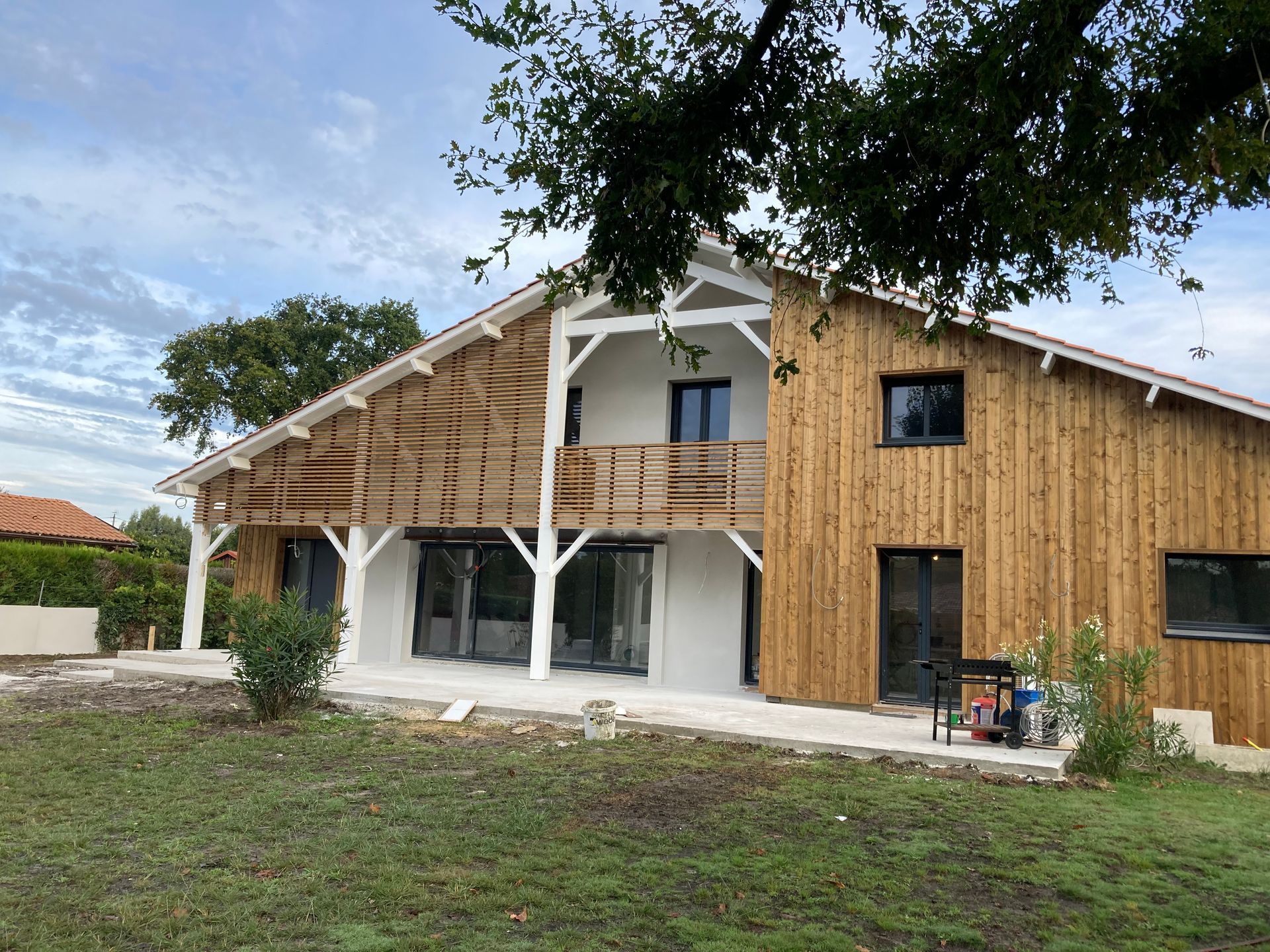 Maison moderne avec bardage en bois et balcon, entourée de pelouse et d'arbres.