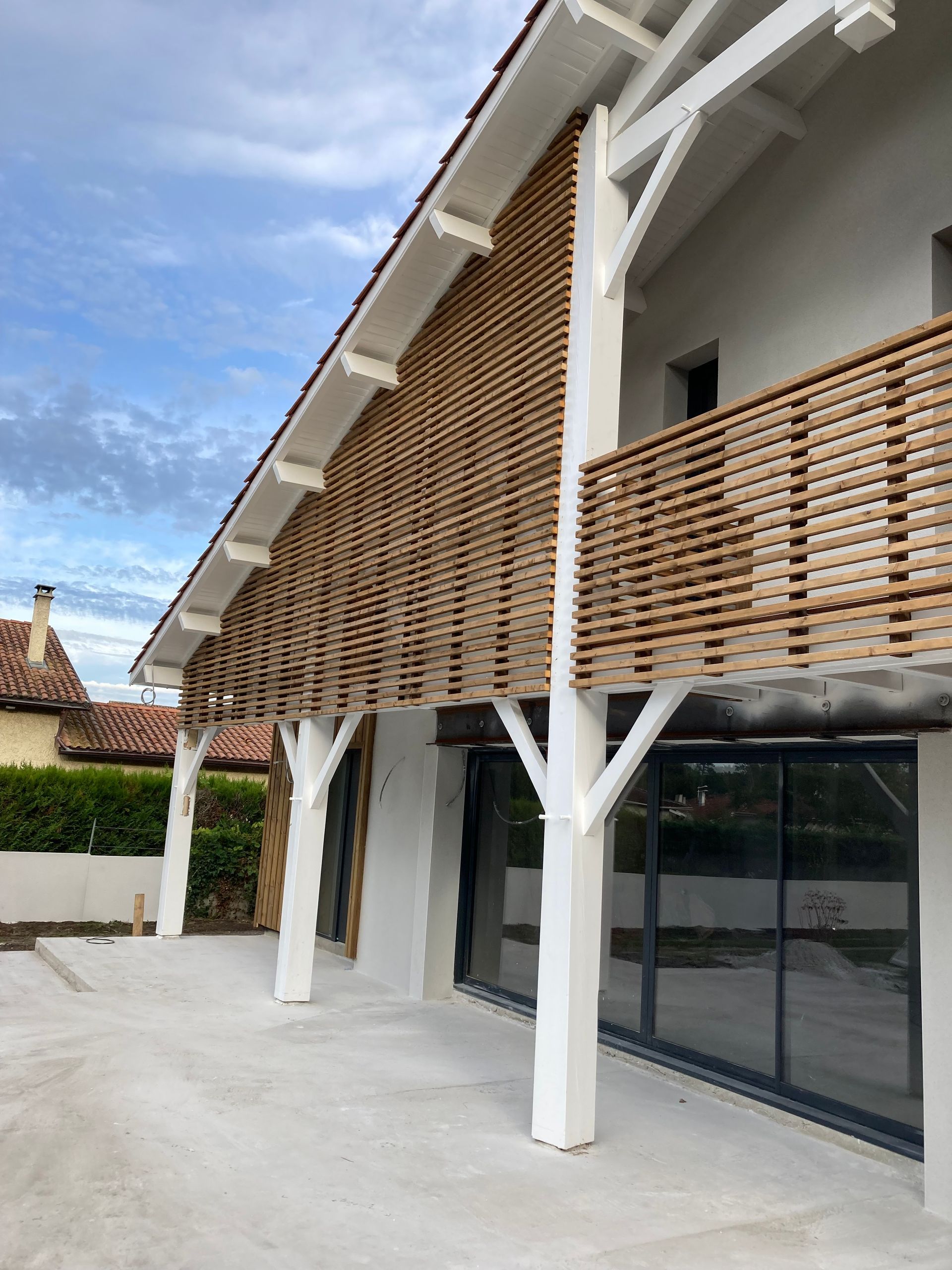 Vue extérieure d'un bâtiment blanc orné de lattes de bois, sous un ciel bleu.