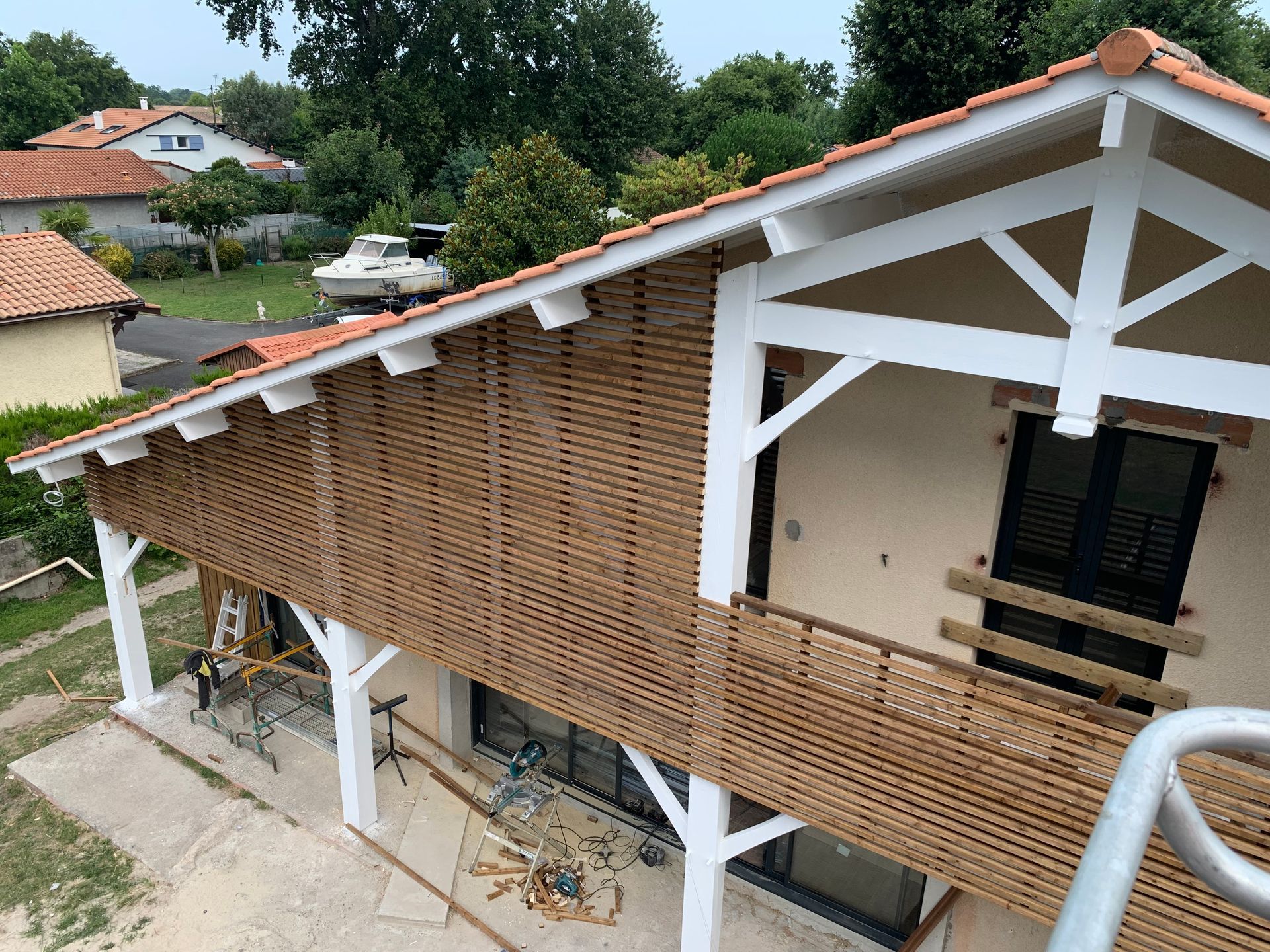 Extérieur d'une maison avec bardage en treillis de bois et boiseries blanches. Matériaux de construction sur une terrasse.