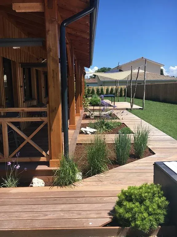 Terrasse et structure en bois avec aménagement paysager et pelouse ensoleillée.