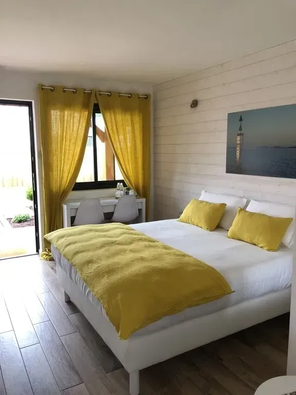 Chambre avec lit blanc, touches de jaune, petit bureau près de la fenêtre et porte ouverte.