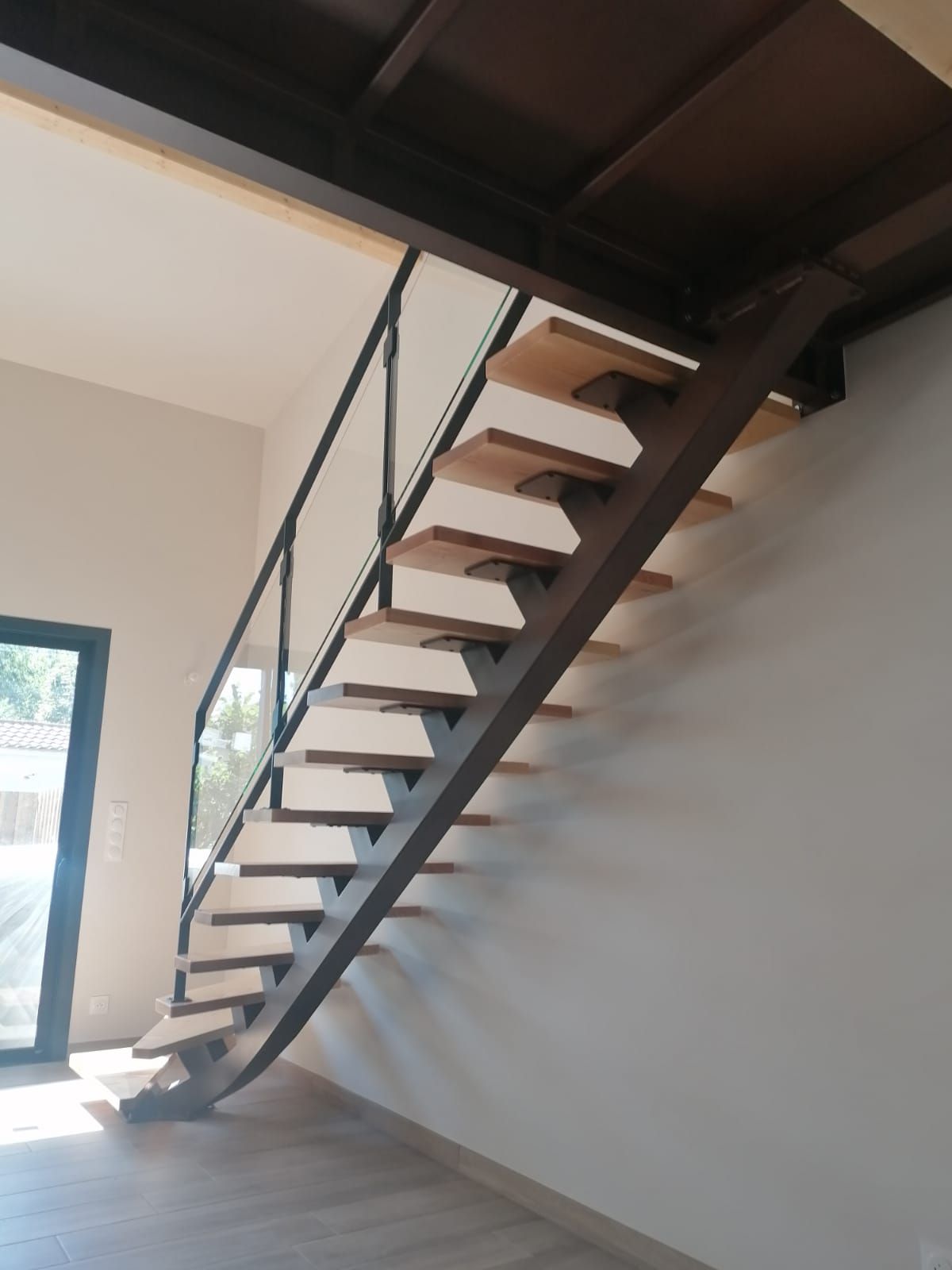 Escalier métallique avec marches en bois, rampe noire et murs blancs.