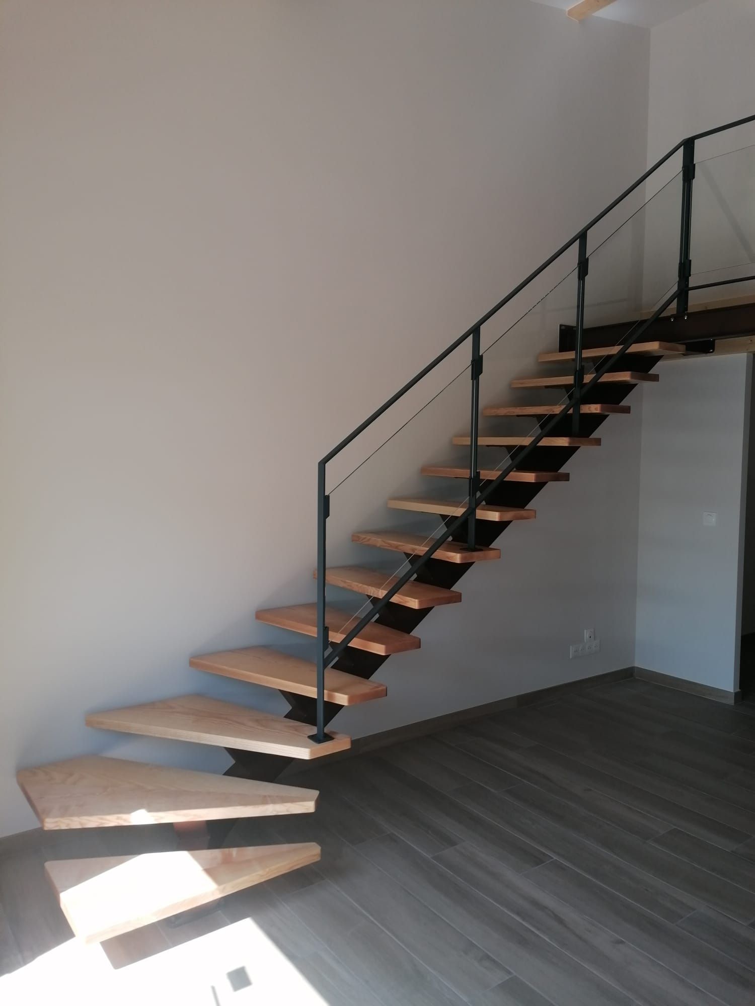 Escalier en bois avec rampe en métal noir dans un intérieur moderne, menant à l'étage supérieur.