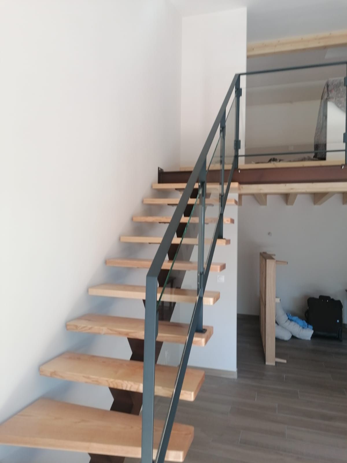 Escalier en bois avec rampes en métal foncé sur des murs blancs.