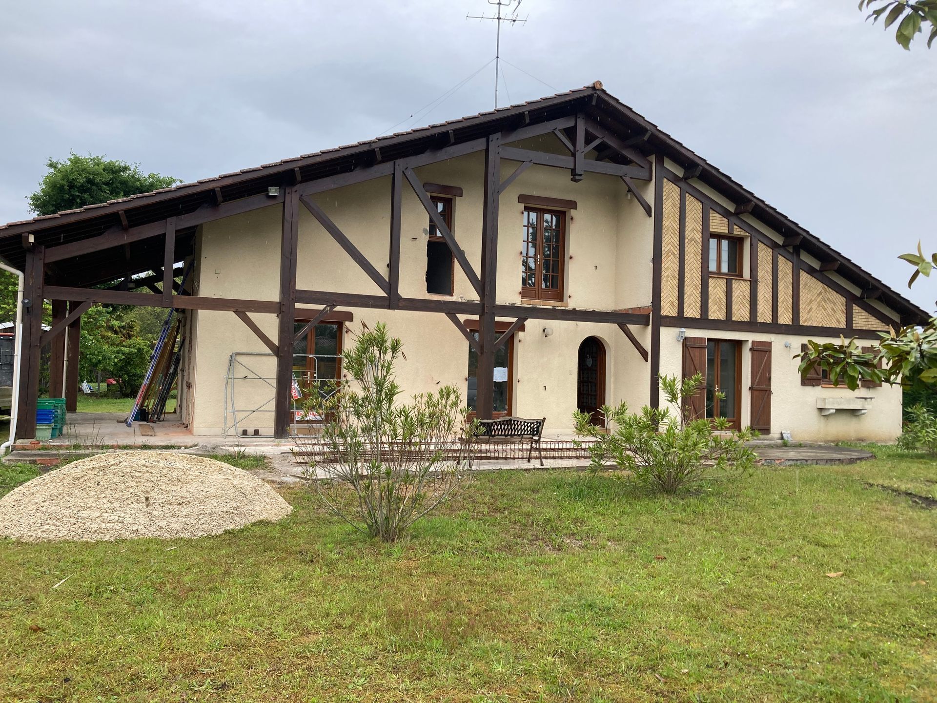 Maison à deux étages avec façade à ossature bois, murs clairs et touches de brun, située sur une pelouse.