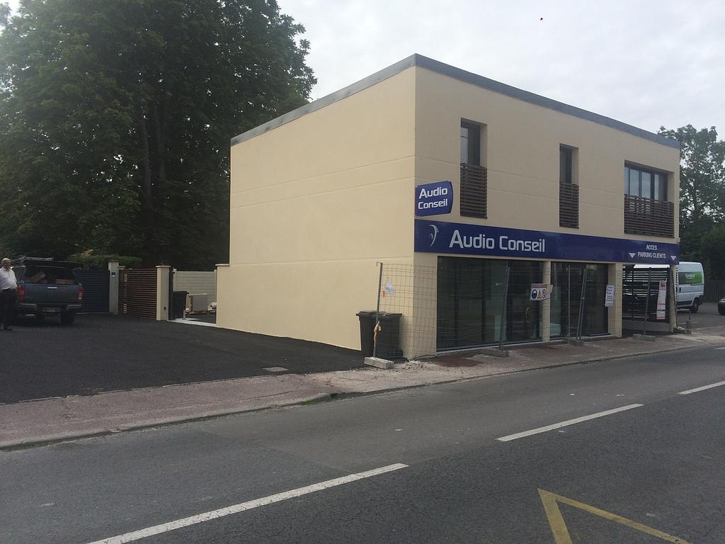 Magasin de pièces automobiles avec une enseigne bleue et un bâtiment beige de deux étages à côté d'une zone pavée.