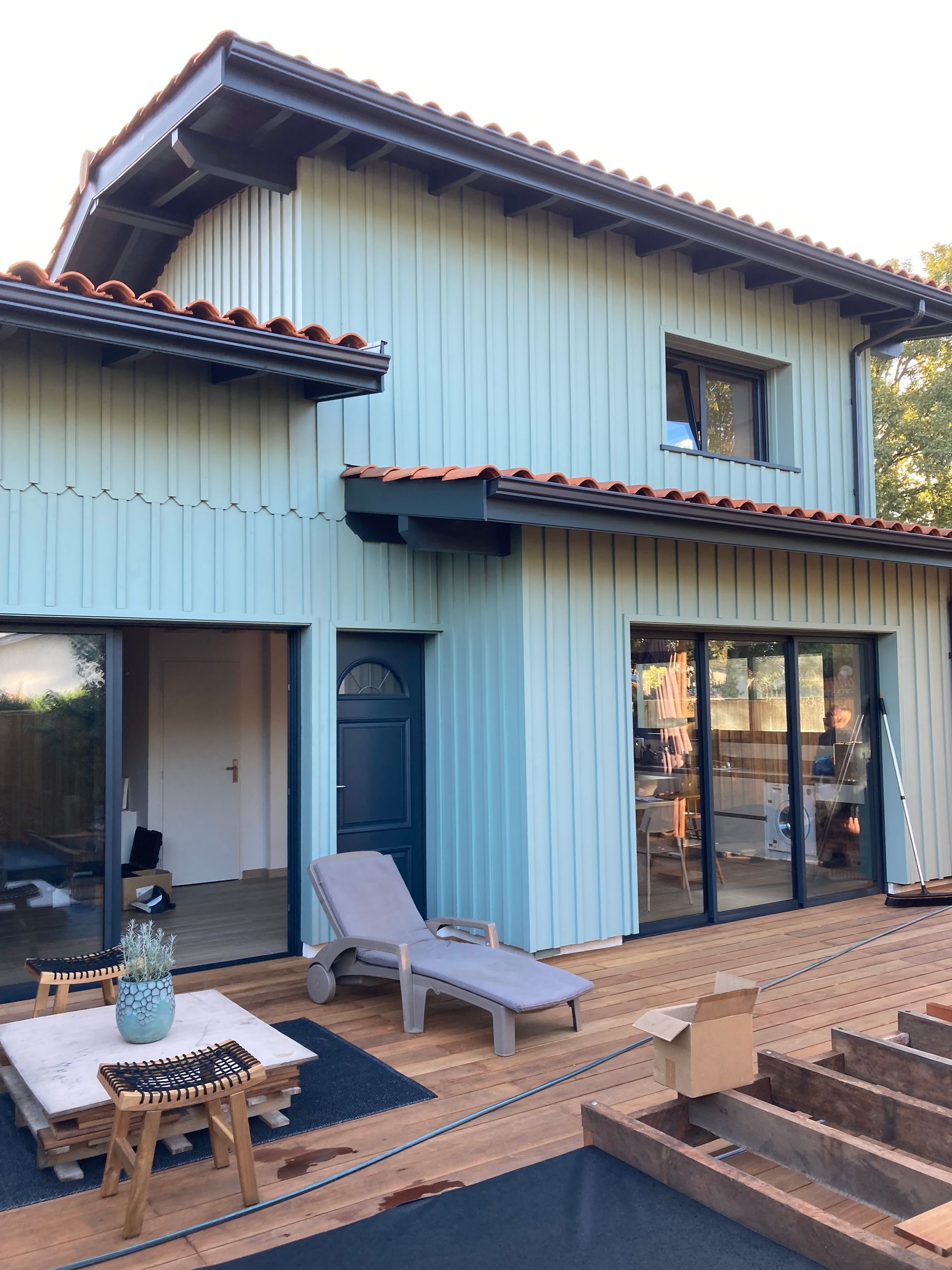 Maison bleu clair avec bardage en bois, boiseries foncées et terrasse.