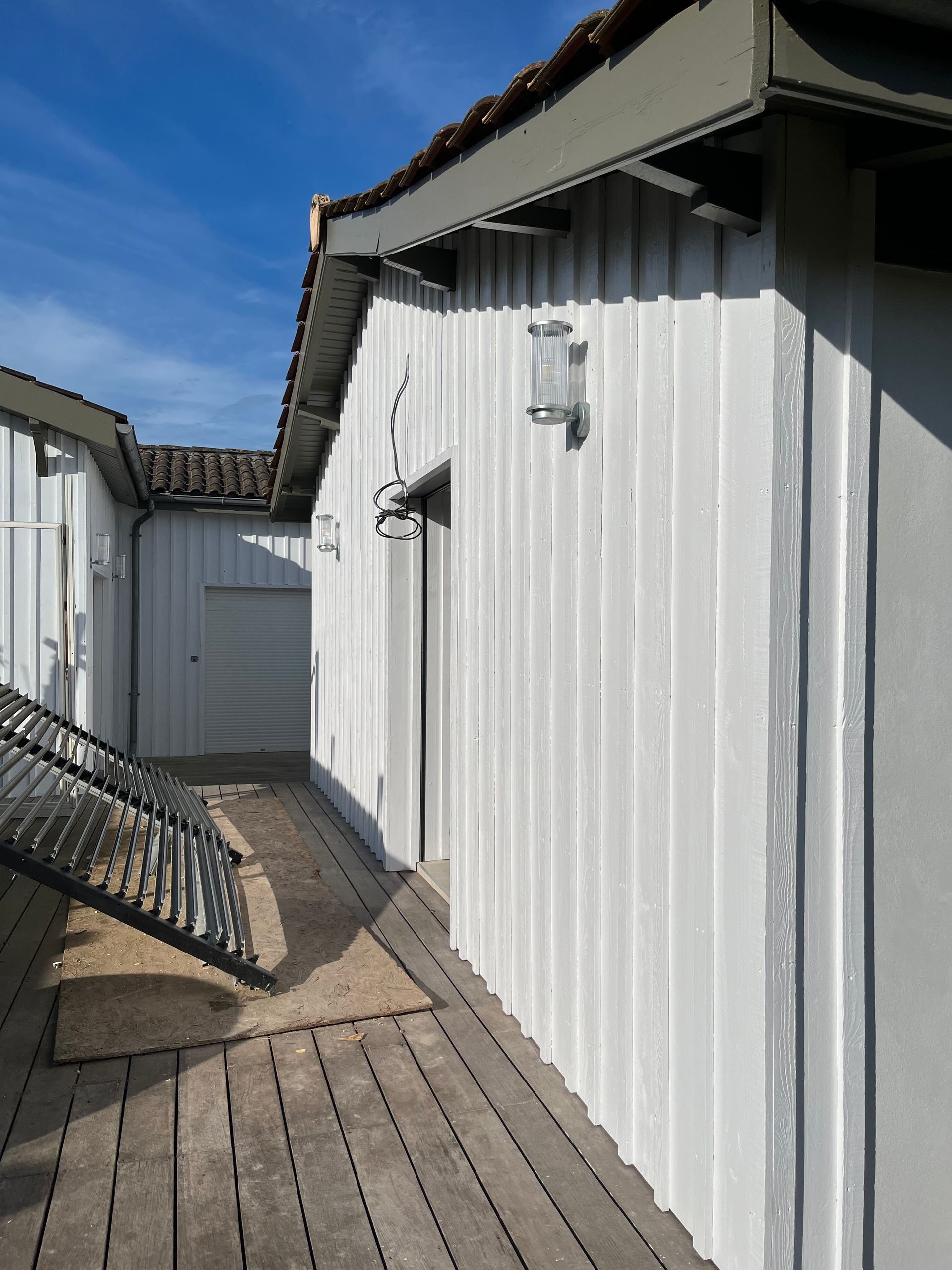 Façade en bois blanc d'un bâtiment avec allée et lumière du soleil.