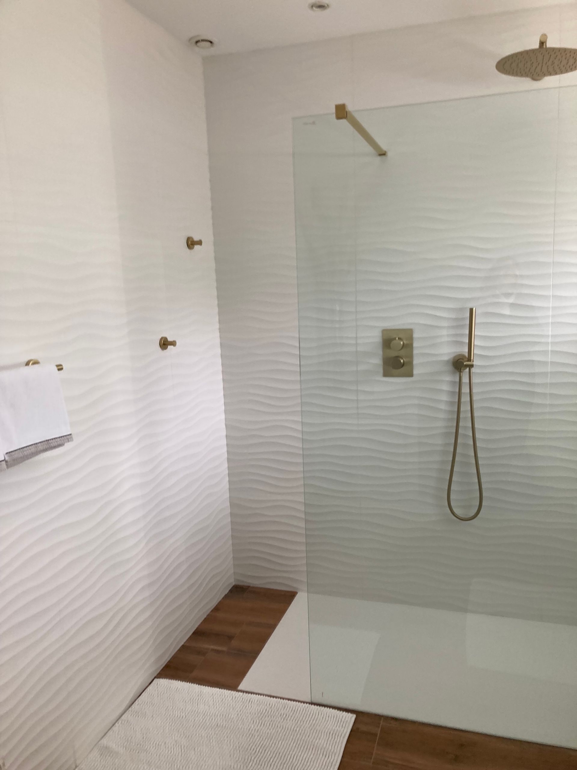 Salle de bains moderne avec carrelage blanc texturé, robinetterie dorée et cabine de douche en verre.