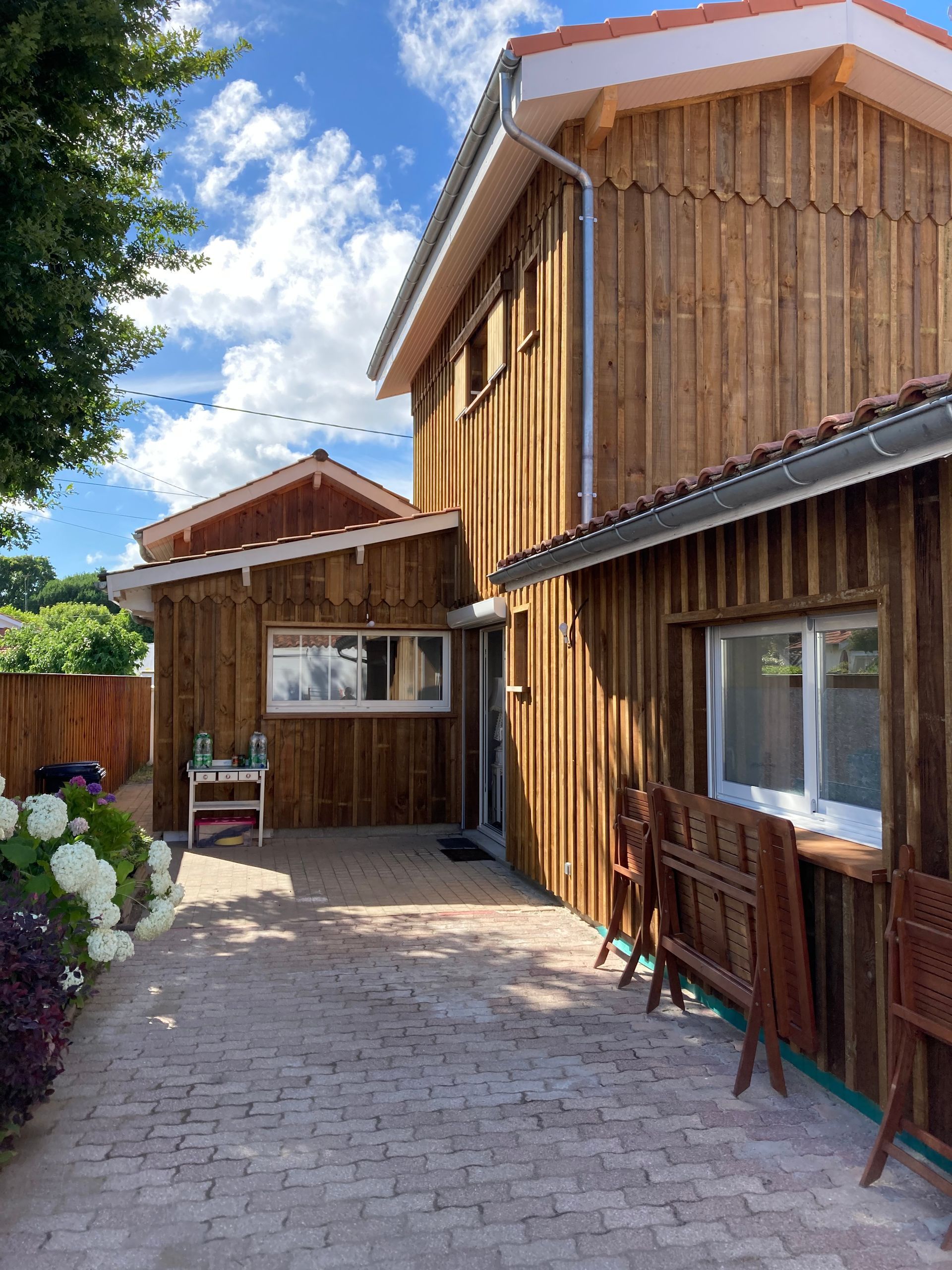 Bâtiments en bois avec chemin pavé et plantes sous un ciel bleu.