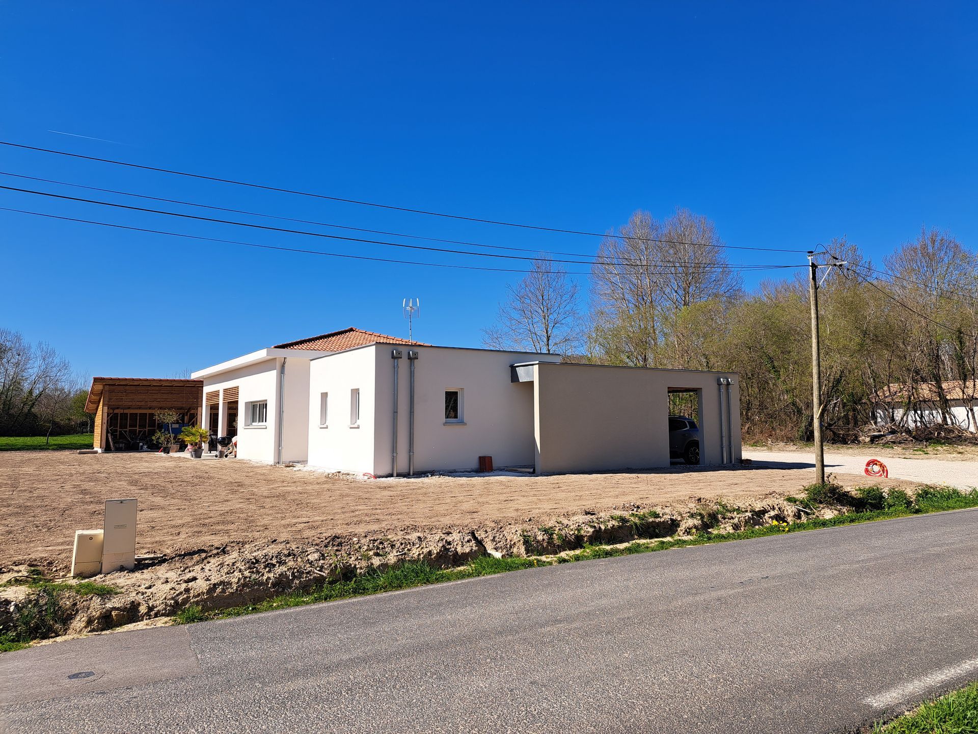 Maison blanche moderne par une journée ensoleillée sous un ciel bleu azur. Terrain vague devant.